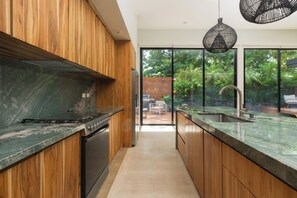 A modern kitchen with wooden cabinets, a marble countertop, and a view of a patio with outdoor furniture. - Spacious 4-bedroom house with AC in marvelous Playa Langosta (Playa Langosta)