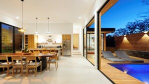 A modern kitchen with wooden cabinets, a dining area with a large table and chairs, and a pool area with lounge chairs. - Spacious 4-bedroom house with AC in marvelous Playa Langosta (Playa Langosta)
