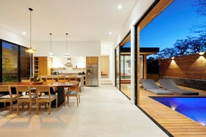 A modern kitchen with wooden cabinets, a dining area with a large table and chairs, and a pool area with lounge chairs. - Spacious 4-bedroom house with AC in marvelous Playa Langosta (Playa Langosta)