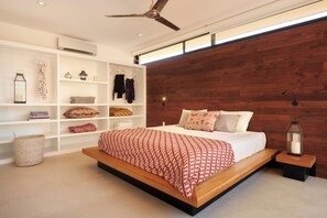 A modern bedroom with a wooden headboard, a large bed with patterned bedding, a white shelving unit with various items, and a ceiling fan. - Spacious 4-bedroom house with AC in marvelous Playa Langosta (Playa Langosta)