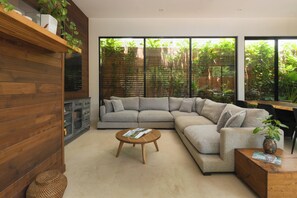 A modern living room with a sectional sofa, a wooden coffee table, and a large window with a view of greenery. - Spacious 4-bedroom house with AC in marvelous Playa Langosta (Playa Langosta)