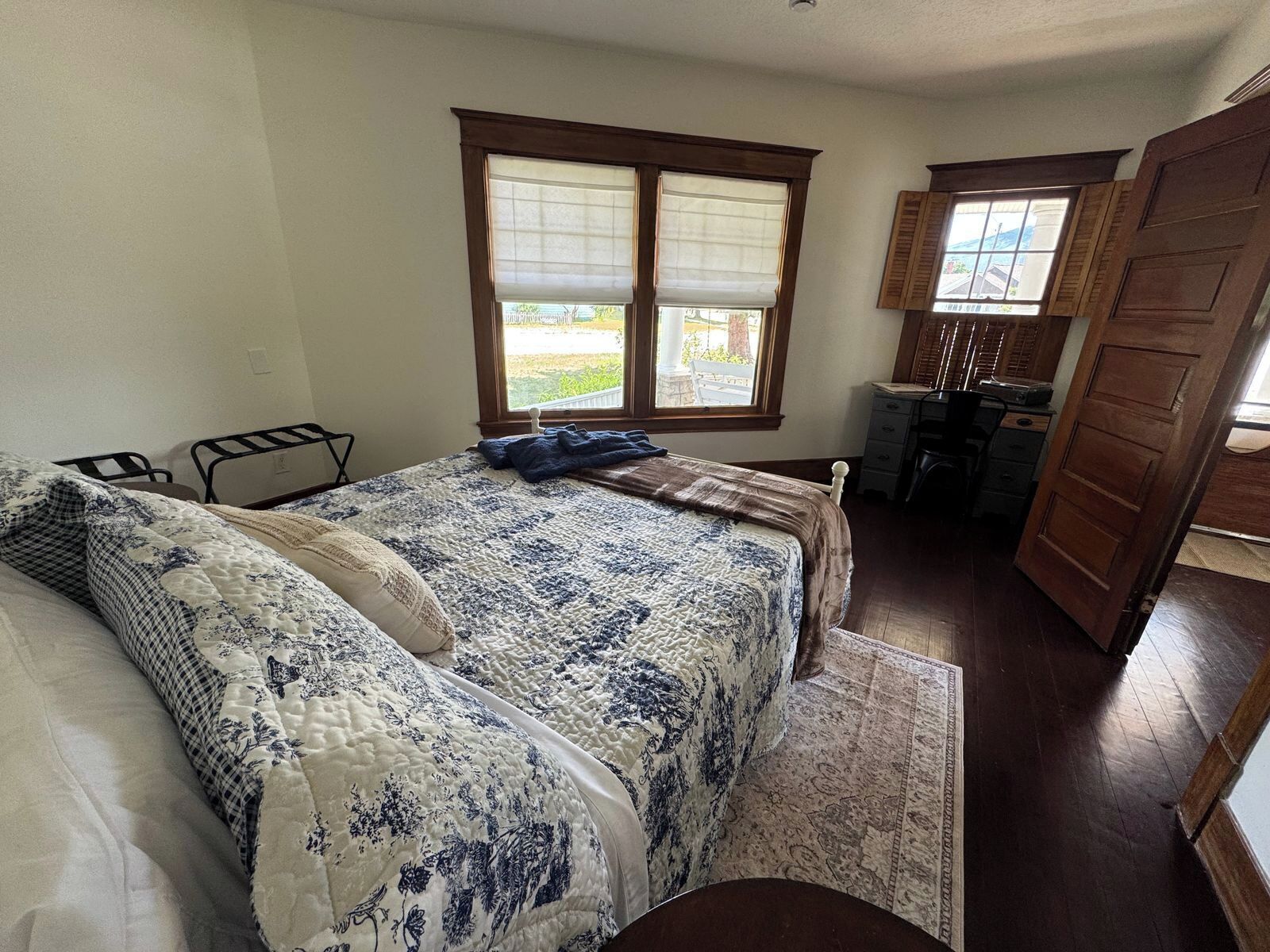 A bedroom with a bed, a desk, and a window with blinds.