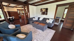 Een woonkamer met een grijze bank, blauwe fauteuils en een kamerkleed met een patroon.