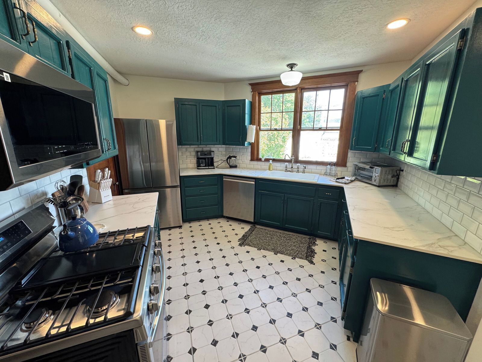 A kitchen with teal cabinets, a stainless steel refrigerator, a microwave, and a gas stove.