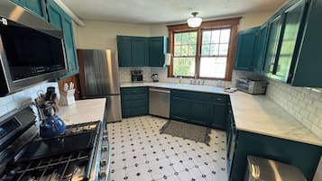 A kitchen with teal cabinets, a stainless steel refrigerator, a microwave, and a gas stove.