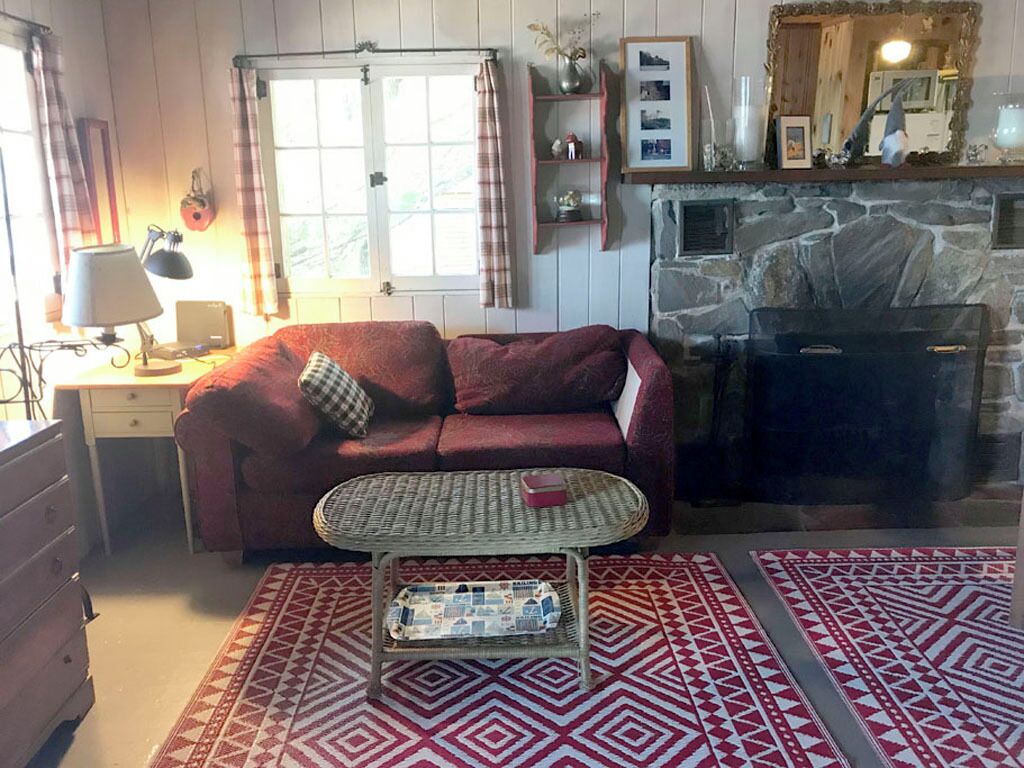 A cozy living room with a red sofa, a wicker coffee table, a fireplace, and a stone wall.