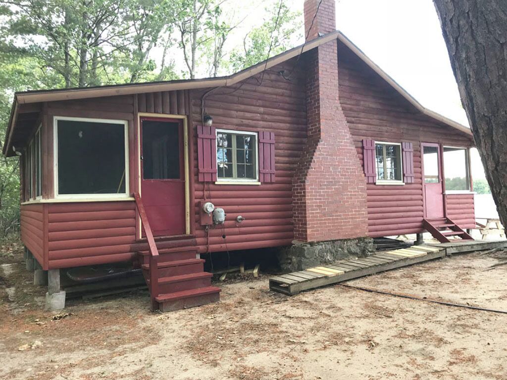 Une cabane rustique dotée d’une cheminée, d’une porte d’entrée et d’un escalier menant à l’entrée.