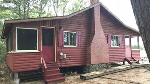 Une cabane rustique dotée d’une cheminée, d’une porte d’entrée et d’un escalier menant à l’entrée.