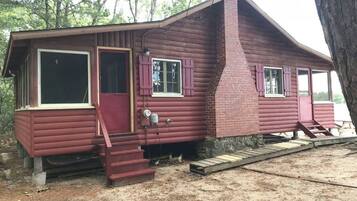 Une cabane rustique dotée d’une cheminée, d’une porte d’entrée et d’un escalier menant à l’entrée.
