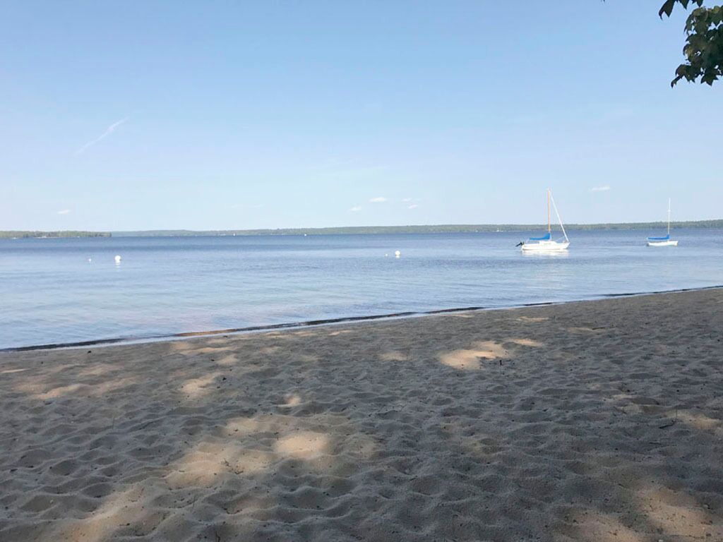 Une plage de sable fin, avec une eau calme et quelques voiliers visibles au loin.