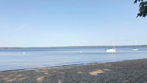 Une plage de sable fin, avec une eau calme et quelques voiliers visibles au loin.