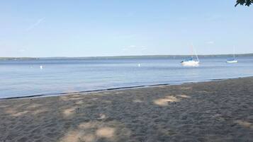 Une plage de sable fin, avec une eau calme et quelques voiliers visibles au loin.