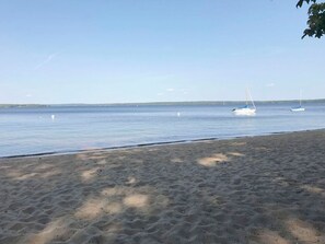 A sandy beach with calm water and a few sailboats in the distance. - Sebago Lake Private Beach Front Classic Cabin (Standish)