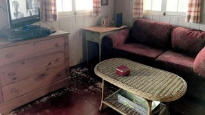 Une pièce comprenant une télévision, un canapé, une petite table, une commode et une fenêtre avec des rideaux.