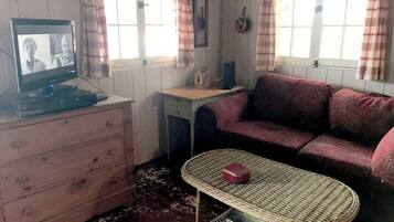 A room with a television, a sofa, a small table, a dresser, and a window with curtains.