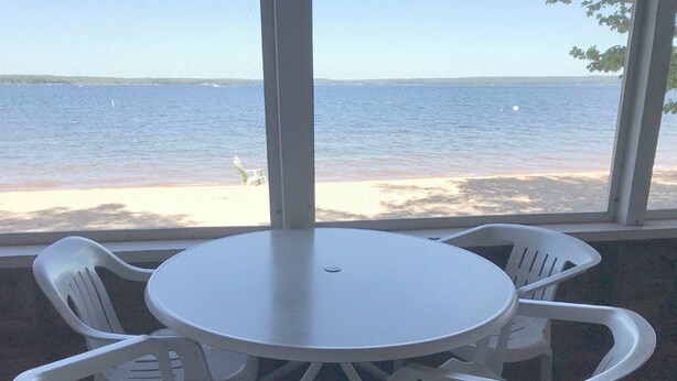 Une table ronde entourée de quatre chaises blanches, avec vue sur la plage et un ciel dégagé.