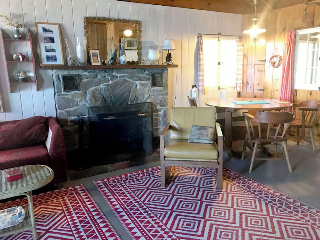 Un salon chaleureux avec une cheminée en pierre, un canapé rouge, un tapis à motifs et un coin repas avec des chaises et une table en bois.