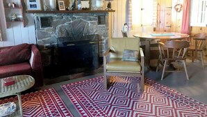 Un salon chaleureux avec une cheminée en pierre, un canapé rouge, un tapis à motifs et un coin repas avec des chaises et une table en bois.