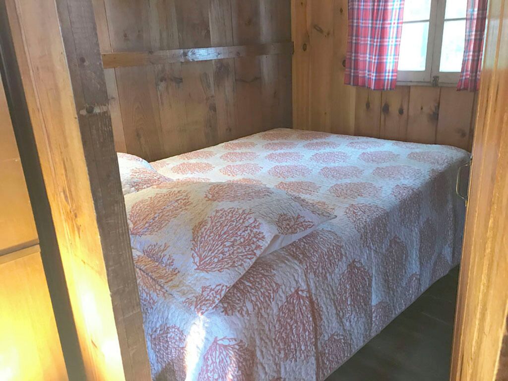 Une pièce de cabane en bois avec un lit, des rideaux à carreaux et une fenêtre.