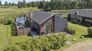 A modern house with a deck, a pond, and a grassy area. - 4 Star Holiday Home in Stubbekobing (Stubbekobing)