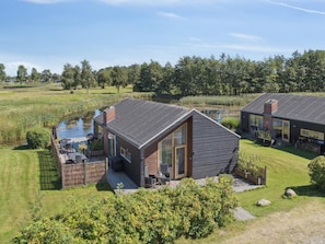 A modern house with a deck, a pond, and a grassy area. - 4 Star Holiday Home in Stubbekobing (Stubbekobing)