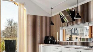 A modern kitchen with white cabinets, a black coffee machine, and a window overlooking a garden. - 4 Star Holiday Home in Stubbekobing (Stubbekobing)