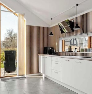 A modern kitchen with white cabinets, a black coffee machine, and a window overlooking a garden. - 4 Star Holiday Home in Stubbekobing (Stubbekobing)
