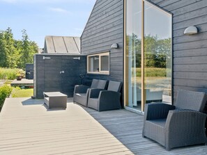 A modern outdoor deck with wicker furniture, a glass door, and a view of the surrounding greenery. - 4 Star Holiday Home in Stubbekobing (Stubbekobing)