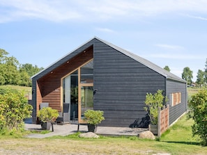 A modern cabin with a sloped roof, large glass door, and a wooden deck. - 4 Star Holiday Home in Stubbekobing (Stubbekobing)