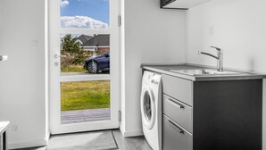 A modern kitchen with a built-in washing machine, a sink, and a door leading to a view of a car and greenery. - "Bilal" - 1.8km from the sea by Interhome (Rømø)