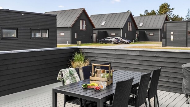 A deck with a table set for dining, surrounded by dark wooden walls and a view of similar buildings. - "Bilal" - 1.8km from the sea by Interhome (Rømø)