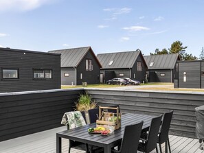 Een terras met een eettafel, omgeven door donkere houten wanden en uitzicht op gelijksoortige gebouwen.