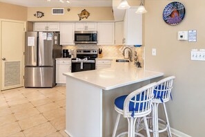 A modern kitchen with stainless steel appliances, white cabinetry, and a central island with bar stools. - 2nd Floor Corner Unit Condo with 3BR, 2BA in beautiful Orange Beach! (Orange Beach)