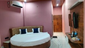Un dormitorio con cama, aire acondicionado, cabecera de madera, televisor montado en la pared y una puerta de madera al fondo.