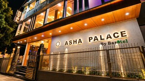 Un hotel llamado 'Asha Palace' con un diseño moderno, destacando una entrada imponente y una fachada bien iluminada.