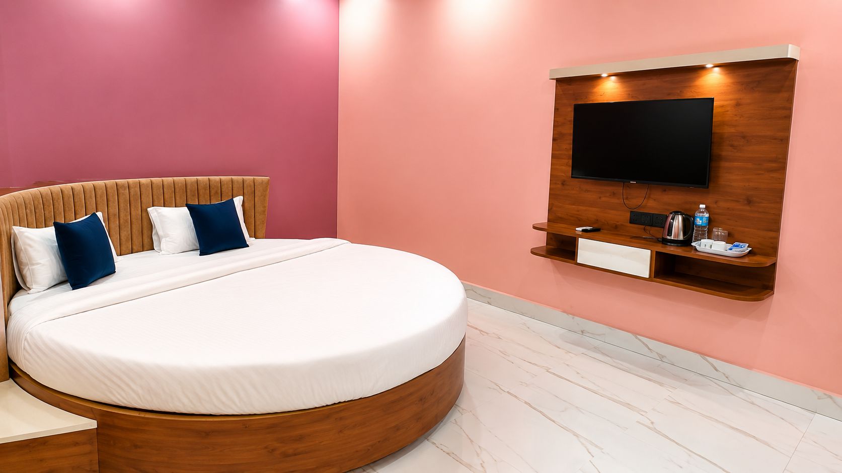 A modern bedroom with a large bed, a TV mounted on a wooden panel, and a small shelf with a kettle and a tray.