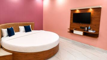 Un dormitorio moderno con una cama grande, un televisor montado en un panel de madera y una pequeña estantería con un hervidor y una bandeja.