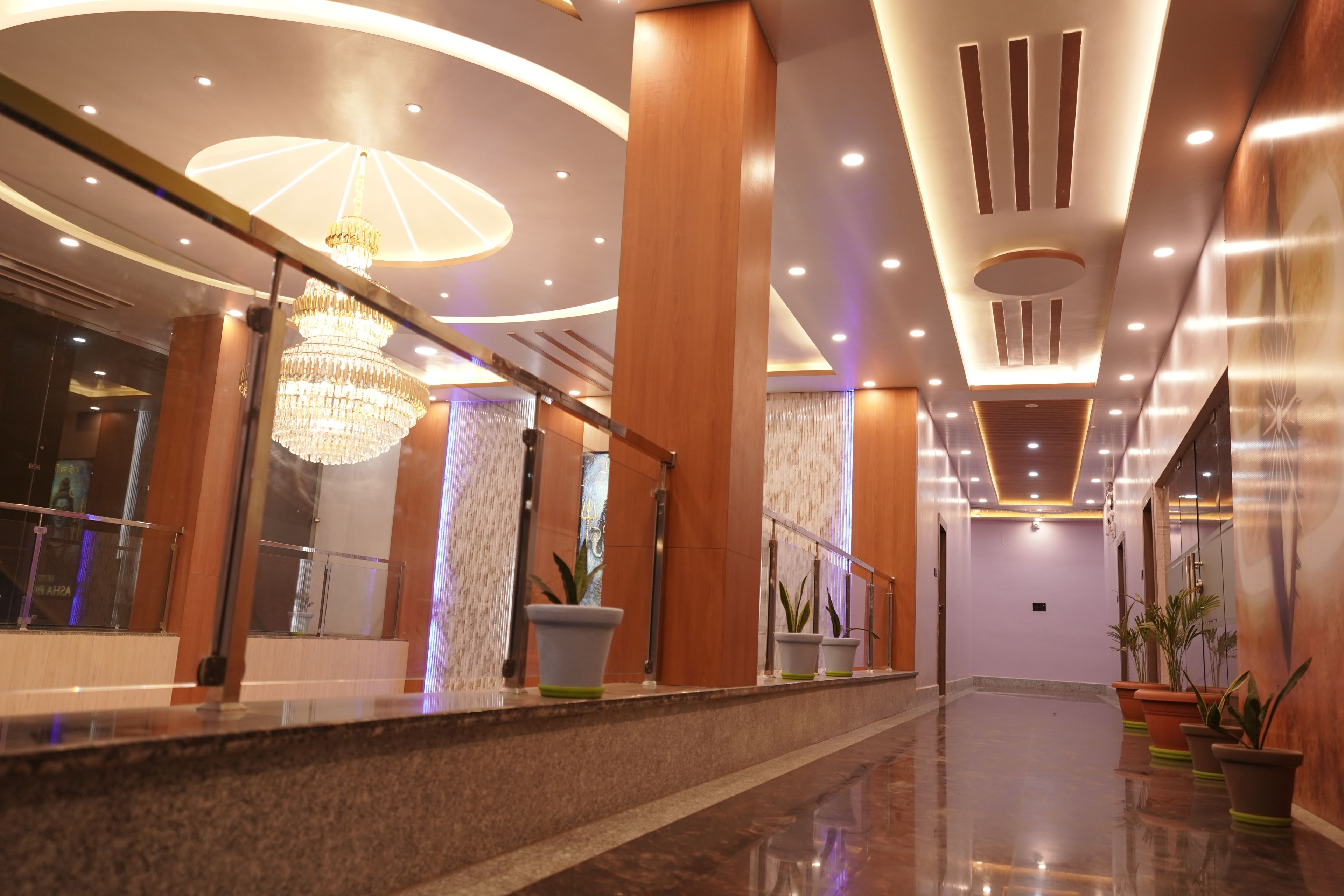 Un moderno vestíbulo de hotel con candelabro, plantas en macetas y suelo de mármol.
