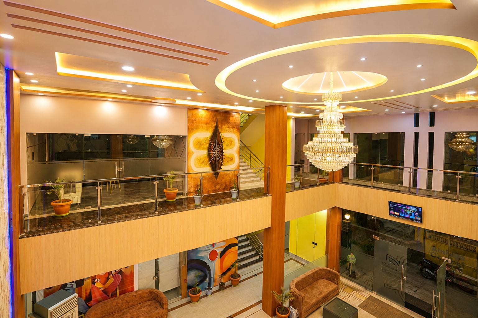 A multi-level hotel lobby with a staircase, a chandelier, and a digital display.