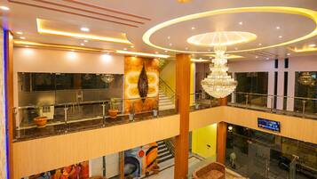 A multi-level hotel lobby with a staircase, a chandelier, and a digital display.