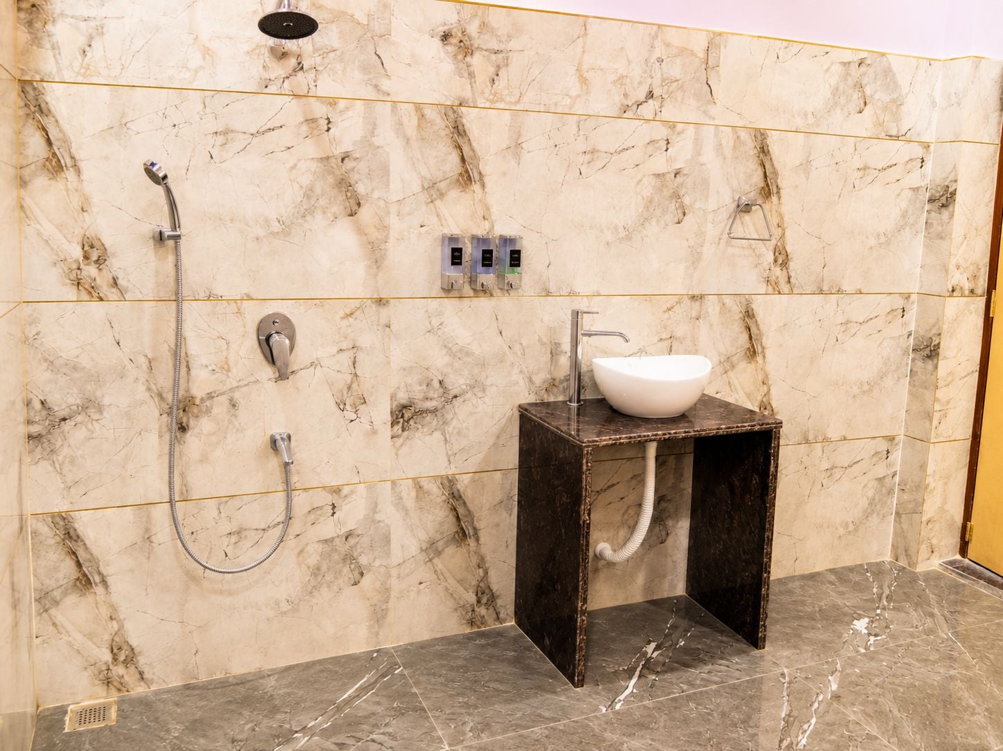 A bathroom with a marble wall, a shower, a sink, and a toilet.