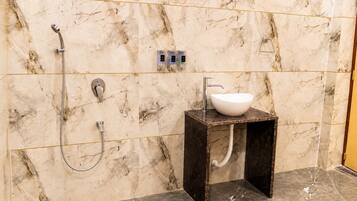 A bathroom with a marble wall, a shower, a sink, and a toilet.
