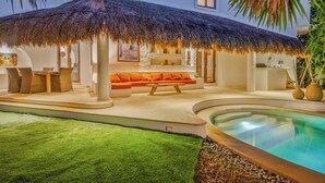 A poolside area with a thatched roof, a sofa, and a dining table. - Beautiful 4-bedroom Villa with Private Pool close to Hotel Zone (Cancún)