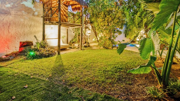 A thatched-roof structure with a bench, surrounded by lush greenery and a well-maintained lawn. - Beautiful 4-bedroom Villa with Private Pool close to Hotel Zone (Cancún)
