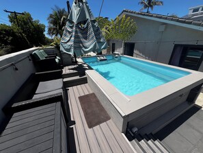 Ein Pool auf dem Dach mit einer Holzterrasse, Liegestühlen und einer überdachten Sitzgelegenheit.