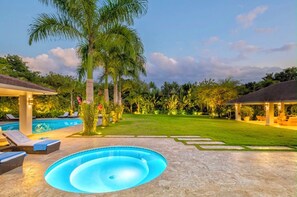 Ein Swimmingpool mit Liegestühlen, einer überdachten Terrasse und einem gepflegten Rasen.