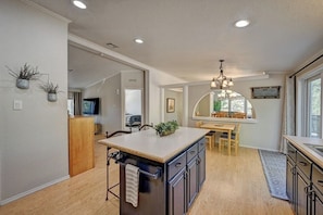 Una cocina moderna con una isla central, suelo de madera y un comedor con vista por una ventana.