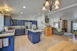 Una cocina amplia con armarios azules, una isla central y una zona de comedor con mesa de madera.