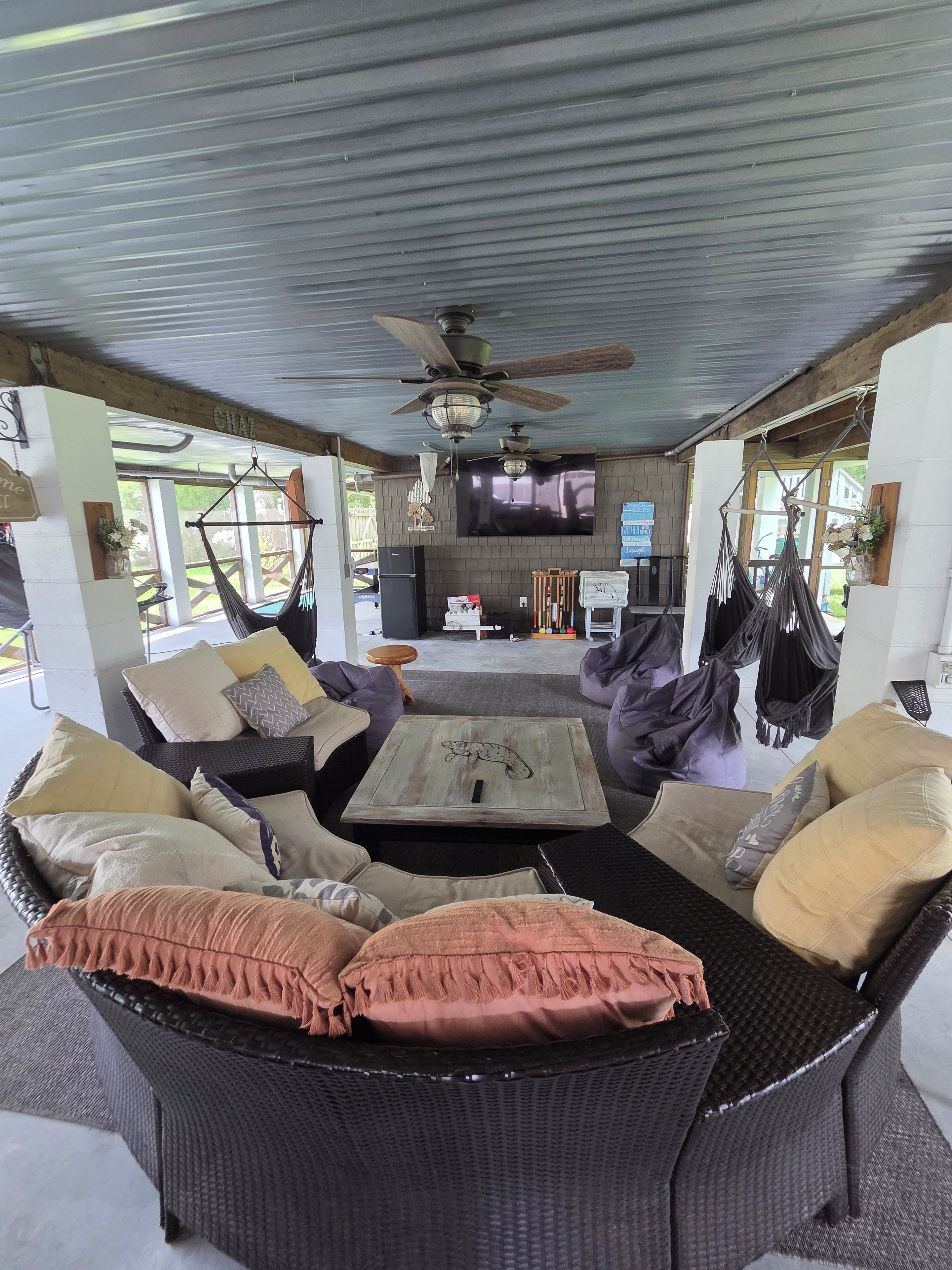 A spacious living area with wicker furniture, a flat-screen TV, ceiling fans, and a view of the outdoors.