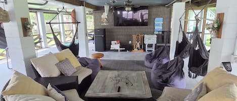 A spacious living area with wicker furniture, a flat-screen TV, ceiling fans, and a view of the outdoors.